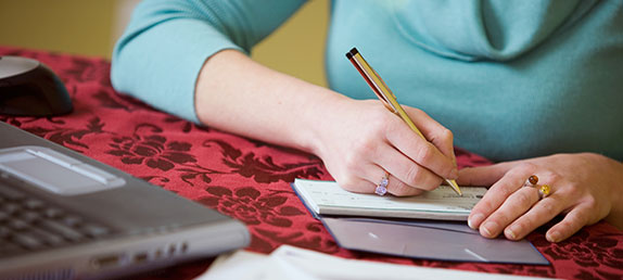 An older woman writing a check to make either a one time or recurring tax-deductible donation to help spread God's word.