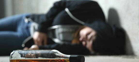A man passed out drunk on a table with an empty bottle of alcohol living in bondage to addiction.
